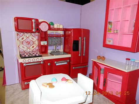 a toy kitchen with red cabinets and pink walls, including a white dining room table