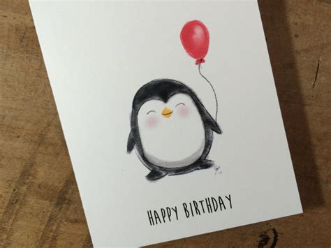 a penguin holding a red balloon on top of a wooden table next to a white card