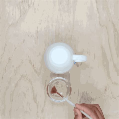 a person holding a spoon over a bowl on top of a wooden table next to a cup