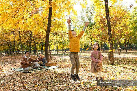 Happy kids playing with autumn leaves while parents resting on checkered plaid in park — nature ...