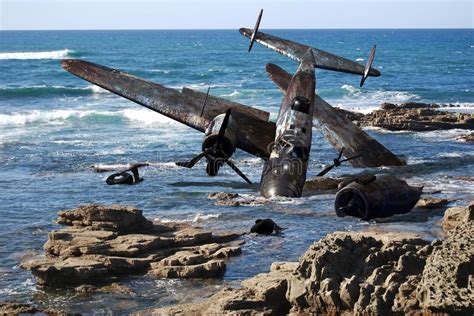 an old plane sitting on top of rocks in the water near the ocean with ...