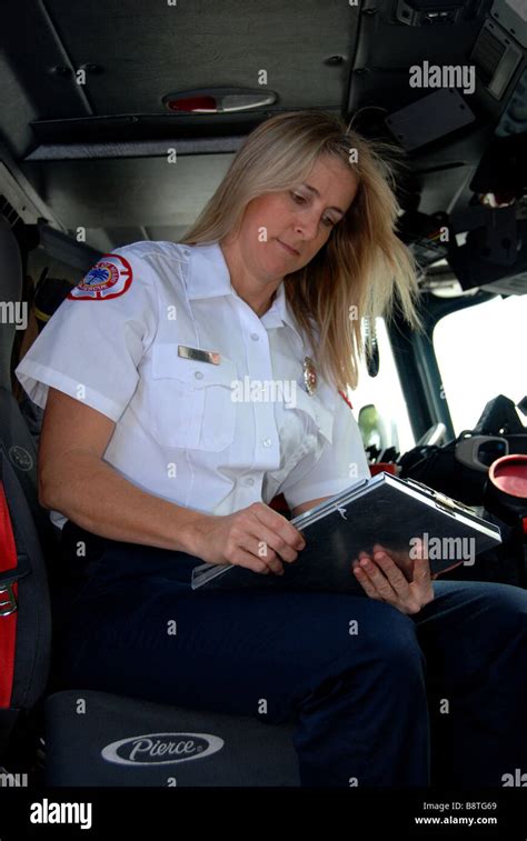 Female firefighter paramedic EMT in dress uniform looking at report sitting in fire engine cab ...