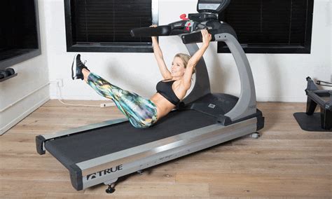 a woman is on a treadmill with her arms in the air and one leg up