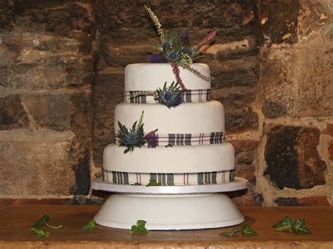 a three tiered wedding cake with flowers on the top and plaid ribbon ...