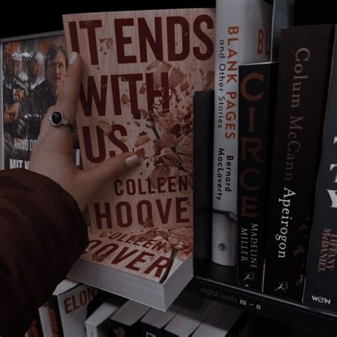 a hand reaching for a book in front of bookshelves with posters on them