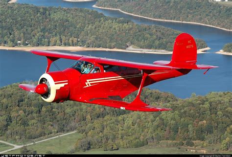 a small red plane flying over a lush green forest next to a lake with lots of water