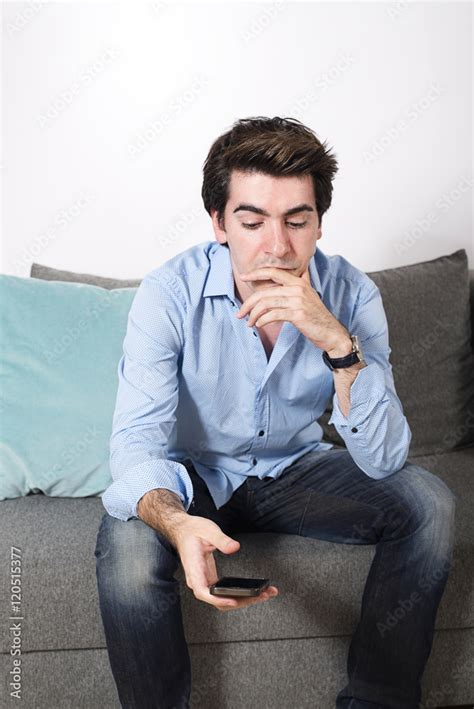 Sad man looking at his phone while sitting on sofa Stock Photo | Adobe ...