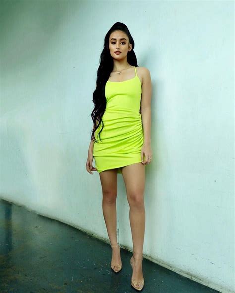 a woman in a short neon yellow dress leaning against a wall with her hand on her hip