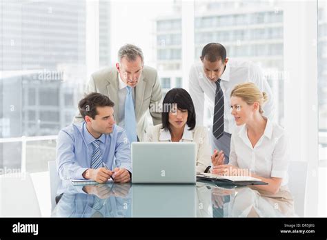 Business people gathered around laptop talking Stock Photo - Alamy