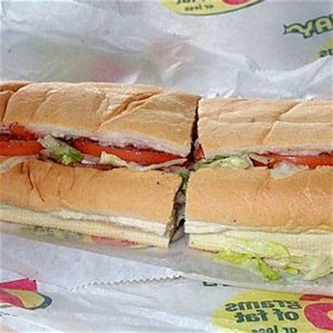 a sub sandwich cut in half sitting on top of a wrapper next to some ketchup