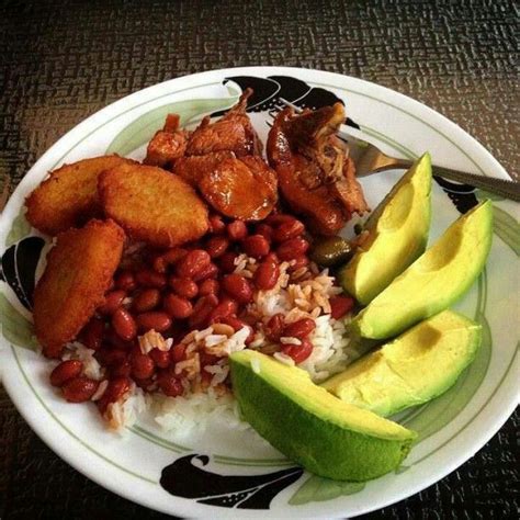 a white plate topped with rice, beans and avocado next to sliced meat