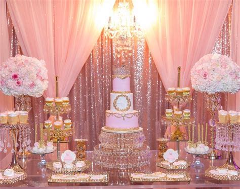 a pink and gold wedding dessert table set up with flowers, candles, cake and cupcakes