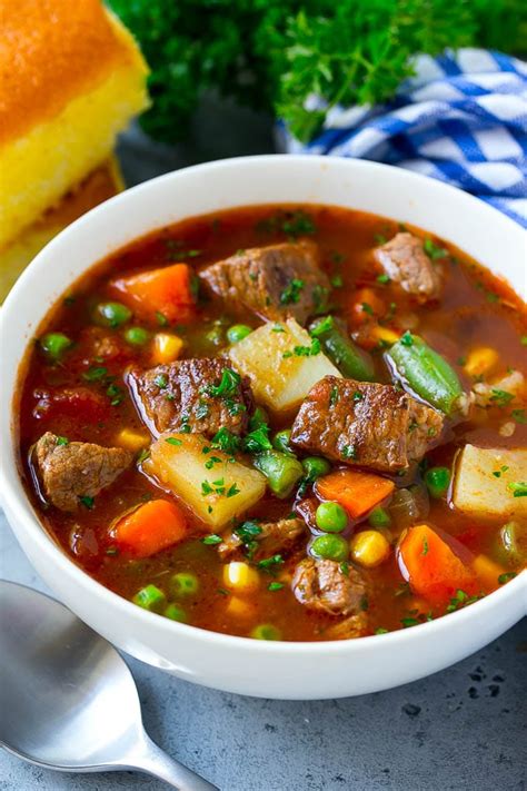 A bowl of vegetable beef soup with carrots, celery, onions, potatoes, tomatoes, corn and peas ...