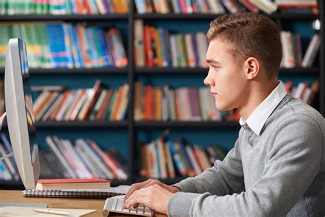 Male Teenage Student Working At Computer In Library • ELC