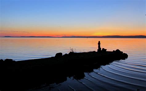 a person standing on the edge of a body of water at sunset