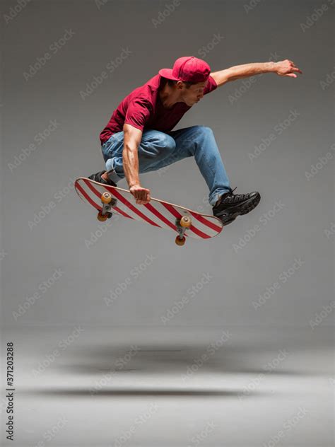 Cool young guy skateboarder jumps on skateboard in studio on grey ...