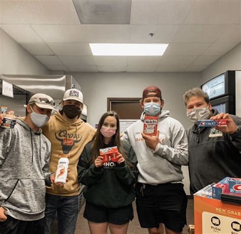 four people wearing masks and holding up boxes of food in front of them, while standing next to ...