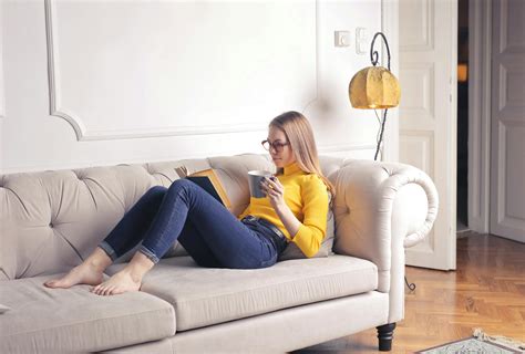 Woman Sitting on White Couch While Reading a Book · Free Stock Photo