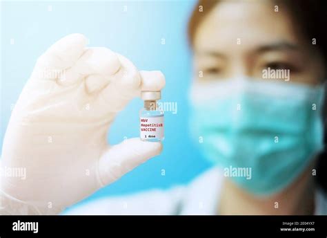 A female Asian physician with surgical mask and white rubber gloves at a clinic, holding a glass ...