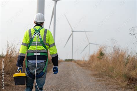 Behind male windmill engineer wearing uniform with helmet safety hold box tools and walking to ...