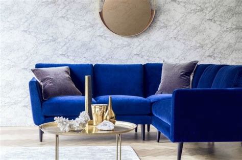 a living room with blue velvet couches and gold coffee table in front of a marble wall