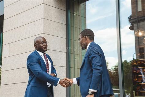 Two black african american businessmen in suits and glasses shake hands while meeting ou in 2023 ...