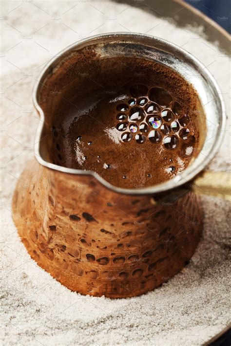 a metal strainer filled with brown liquid on top of a white plate covered in sand