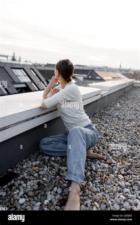 barefoot woman in jeans sitting on rooftop and looking away Stock Photo - Alamy