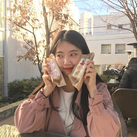 a woman sitting at an outdoor table holding two small sandwiches in front of her face
