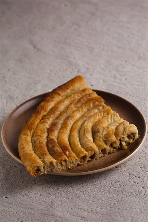 Quarter of a burek pie on a plate on gray background.