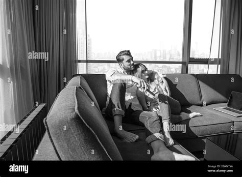 Young couple sitting on sofa near the window watching television together at luxury home Stock ...