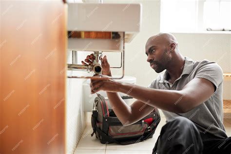 Premium Photo | Young black male plumber sitting on the floor fixing a ...