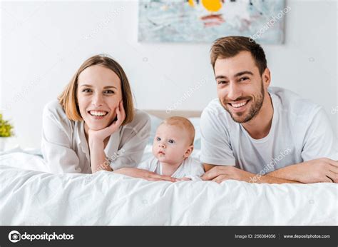 Smiling Young Parents Baby Lying Bed Looking Camera Stock Photo by ...