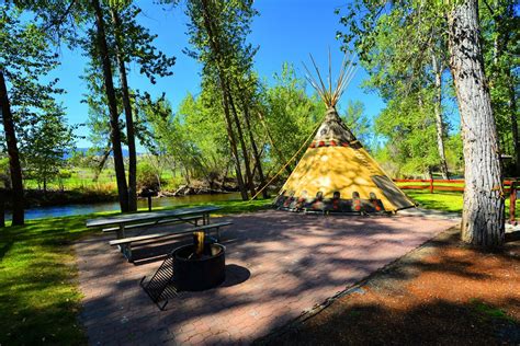 a teepee sitting in the middle of a park next to a river and trees