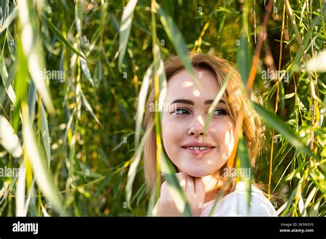 Cute woman smiling under willow tree in sunlight with shadow from ...