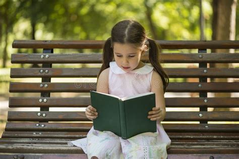 Little Girl Reading a Book Sitting on a Bench in the Garden Stock Image ...