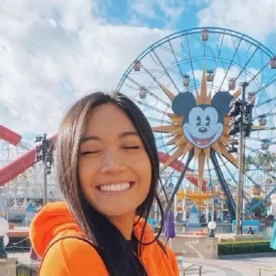 a woman taking a selfie in front of a mickey mouse ride at an amusement ...