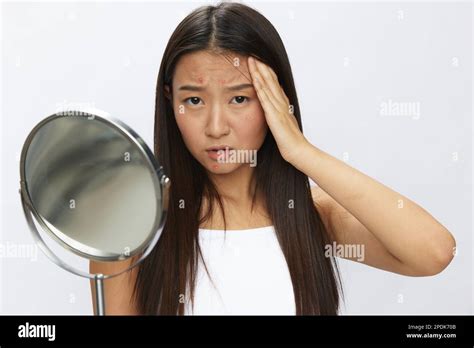 Femme asiatique avec miroir dans la main problèmes de peau faciale, acné et inflammation ...