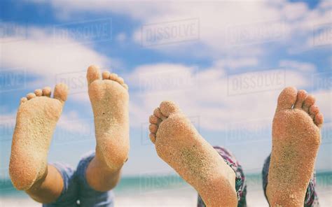 Close-up of two pairs of feet on beach covered in sand - Stock Photo - Dissolve