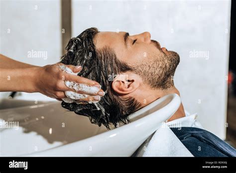 close-up partial view of hairstylist washing hair to handsome young man ...