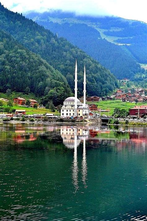 a large white building sitting on top of a lake next to green hillside ...