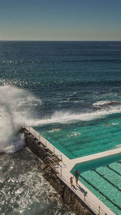 two people are standing on the edge of a swimming pool as waves crash into the water