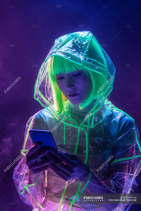Young asian woman in futuristic wear and green wig using smartphone in fluorescent light ...