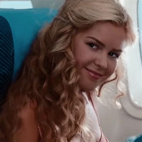 a woman with long blonde hair sitting on an airplane looking at the camera and smiling