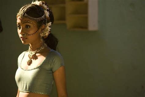 a woman in a green shirt and headpiece standing next to a wall with a clock on it