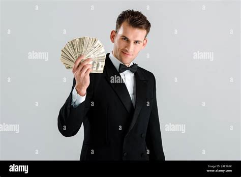 happy and rich man in suit holding dollar banknotes isolated on grey ...