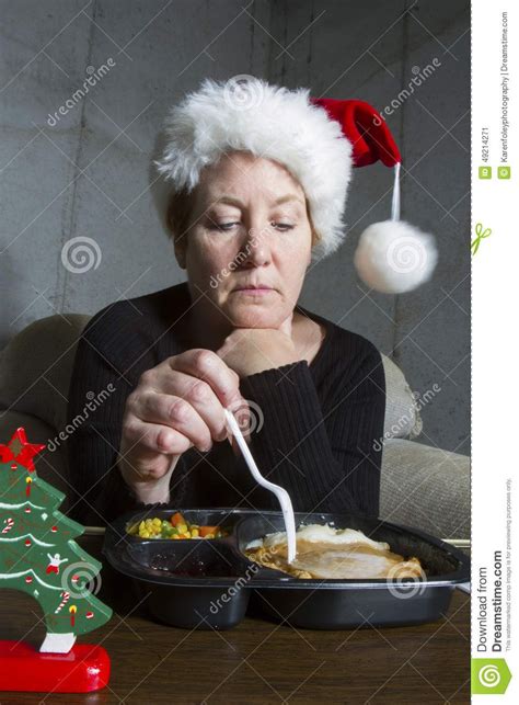 Unhappy woman wearing a christmas stocking hat eating a turkey TV dinner on a tray table in the ...