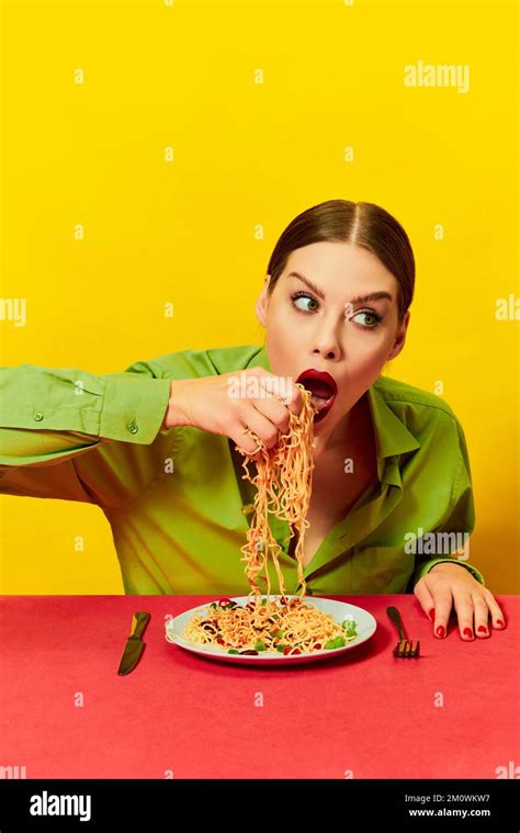 Emotional young girl eating spaghetti, noodles with hands on red tablecloth over yellow ...