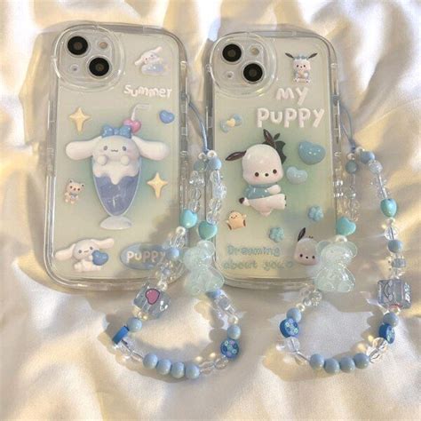 two cell phones with charms attached to them sitting on a white sheet covered bed next to each other