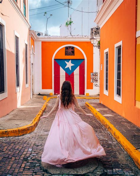 a woman in a pink dress walking down an alley way with a puerto rican flag painted on the wall ...